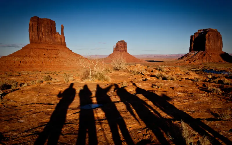 A group of solo travellers cast shadows on the floor of Monument Valley, USA
